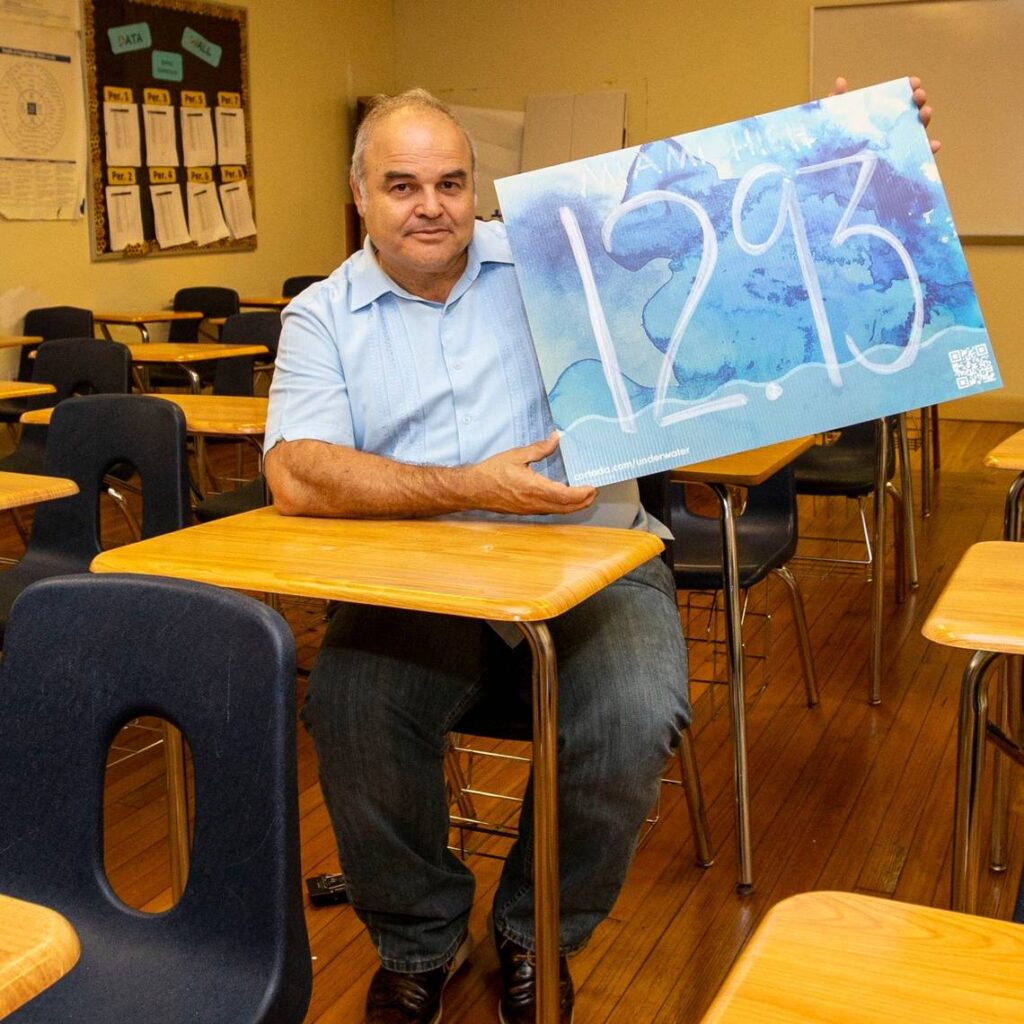 Cuban artist Xavier Cortada holds up a yard sign marked with the elevation of Miami Senior High in Miami, Florida, on Tuesday, April 5, 2022.